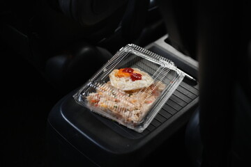 A clear lunch box containing a fried egg, set in a car.