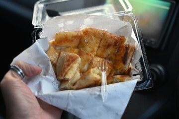 Eating in the car, holding a box of roti with a plastic fork
