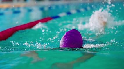 A determined swimmer in a vibrant pink cap and goggles showcasing her strength and focus in the water, captured throughout her training session in the pool.