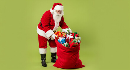 Traditional Santa Claus with a large red sack overflowing with wrapped Christmas gifts on a solid green studio background