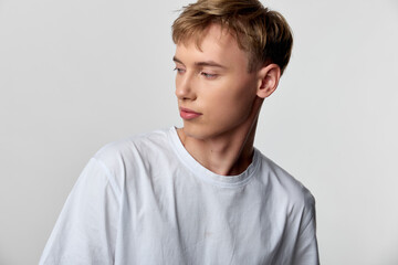 Man in a white shirt gazes pensively to the side in a clean studio setting, minimal background, soft lighting, casual mood, modern style, calm and reflective
