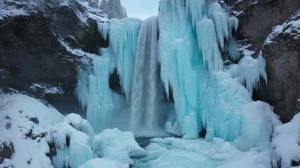 Spectacular frozen waterfall in a winter wonderland surrounded by ice formations and snow-covered cliffs creating a breathtaking natural icy landscape - Powered by Adobe