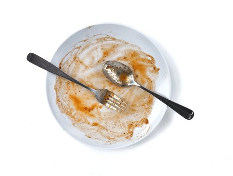 Dirty white plate with leftovers food with spoon and fork on top isolated on white background. Flat lay 