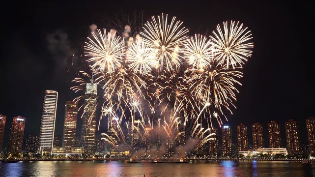 A vibrant fireworks display illuminates a modern city skyline at night. Colorful explosions over the water for a New Year or holiday celebration. Festive urban event