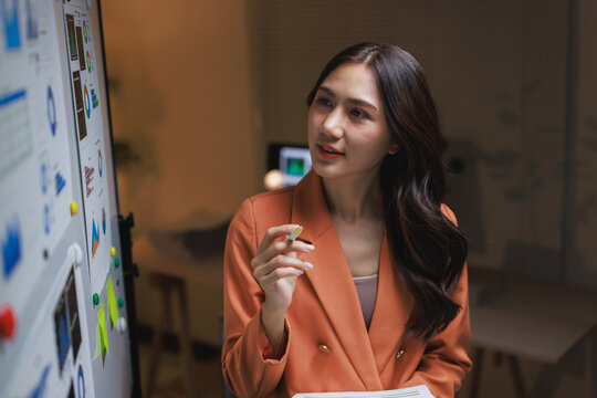Asian businesswoman analyzing data on office whiteboard