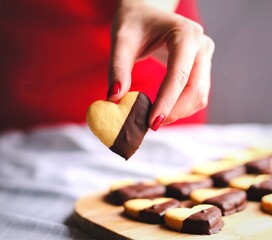 Hand holding a heart shaped cookie dipped in chocolate