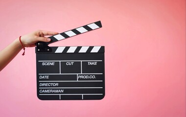 Hand holding a movie clapperboard against a pink background