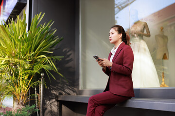 Young businesswoman using smartphone while sitting outside building