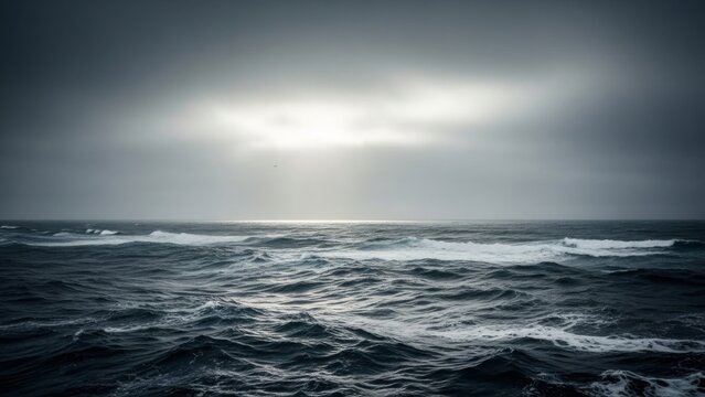 Dramatic seascape featuring dark, choppy ocean waves under a cloudy, overcast sky with sunlight breaking through.