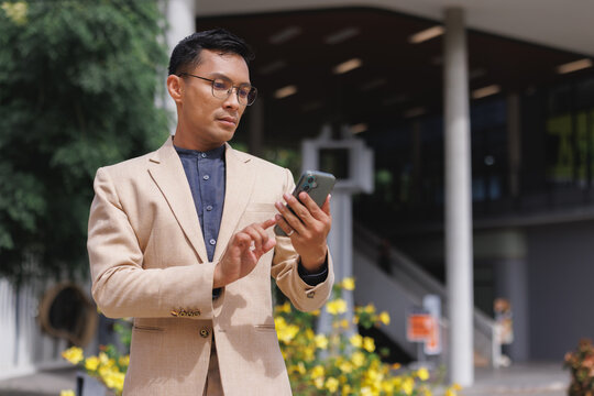 Asian businessman using smartphone outdoors for communication - Powered by Adobe