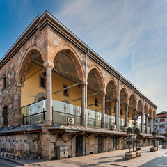 Fototapeta premium Ottoman-era Kapu Mosque exterior, Konya, Turkey. Historic stone architecture with multiple arches, ornate ceilings, and a long facade under a clear blue sky