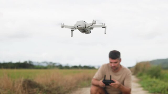 Middle aged man controls drone. It is hobby for outdoor recreation. Drone hovers impatiently above ground. Man examines drones control panel. Fascination with modern technology.