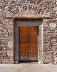 Fototapeta premium Double wooden door set in a textured stone wall with an arched stone lintel at Alaeddin Mosque, Konya, Turkey. Historic architecture detail