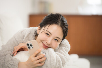 冬のモコモコした部屋着で寝転がるスマホを見る若い女性カメラ目線