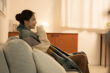 A young woman drinking a hot beverage in a room lit by nighttime lamps Winter image of a woman