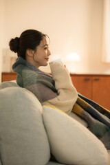 夜の灯りの部屋でホットドリンクを飲む若い女性　女性の冬イメージ　白熱灯のあたたかいイメージ