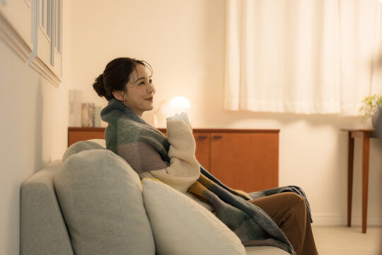 夜の灯りの部屋でホットドリンクを飲む若い女性　女性の冬イメージ　白熱灯のあたたかいイメージ