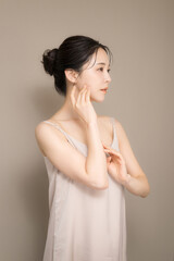 髪の毛がアップ背景がベージュの使いやすい美容やスキンケアの美しい女性のイメージ上半身　手で頬を触る横顔