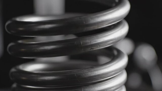 Extreme close-up cinematic shot of a silvery metallic spiral coil spring slowly extending and retracting creating rhythmic mechanical motion background footage, extreme close-up, slowly extending