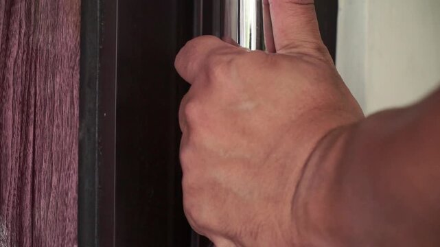 Human hand turning and pulling a shiny door handle to open a wooden door. Detailed close-up showing texture of skin and door material.