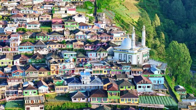 Drone footage of a traditional Indonesian village featuring colorful rooftops, a mosque with twin minarets, and terraced farmlands on the hillside. Nepal Van Java.