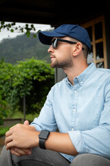 Fototapeta premium Man wearing sunglasses and cap sits thoughtfully by vineyard