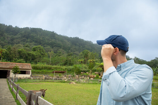 Man looking towards a ranch area with grassy field and animals - Powered by Adobe