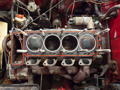 Open, inline four engine block with head gasket, exposed cylinders with carbon deposits or buildup and removed cam cover. Top down, close up shot, no people
