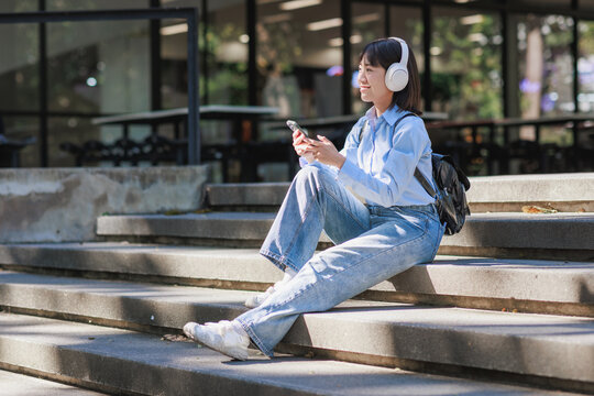 Young woman enjoying music outdoors sitting on campus steps - Powered by Adobe