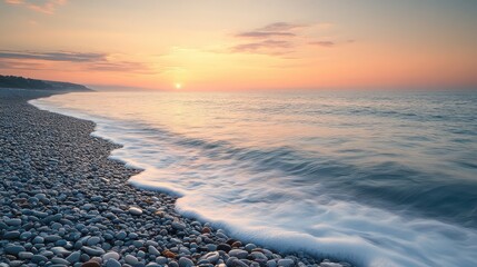 A pebble beach meeting the ocean water at a hazy sunset time