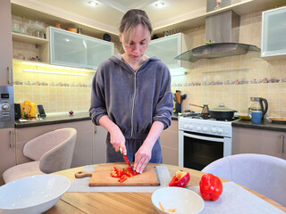 Young woman in kitchen cutting red pepper on wooden board