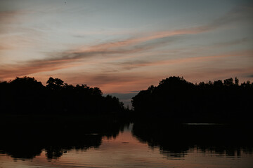 Fototapeta premium Sunset reflecting on calm lake water with dark forest silhouette