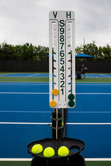 Scoreboard and tennis balls on net post with player in background. © Cavan