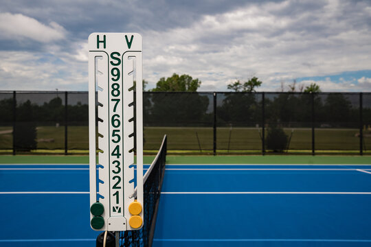 Scoreboard on center net of empty blue tennis court outdoors.