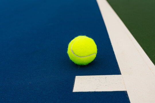 Single yellow tennis ball on blue court near white line edge