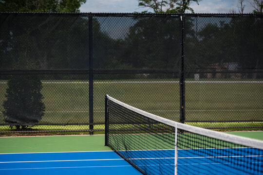 Empty tennis court with net and surrounding chain-link fence.