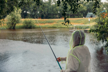 person fishing in the rain by a lake. trees and house