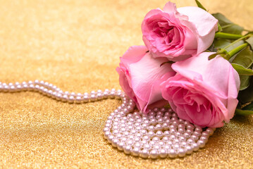 Pink rose and pearl necklace on a shiny gold background
