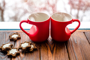 two heart shaped mugs with tea on the background of a window in winter