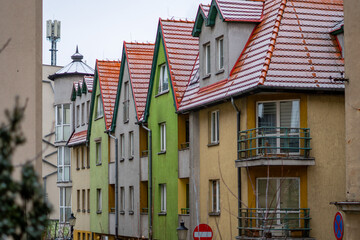 Colorful townhouses with red snow-dusted roofs create a winter urban streetscape featuring distinctive residential architecture and vibrant building facades