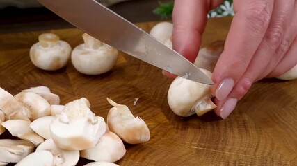 Slicing fresh white button mushrooms with a knife on a wooden cutting board for a recipe