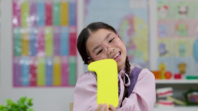 Young Student Holding Number One in Colorful Classroom