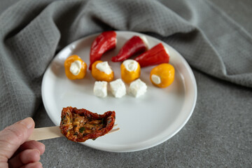 hand holding roasted seasoned tomato on wooden fork over appetizer plate