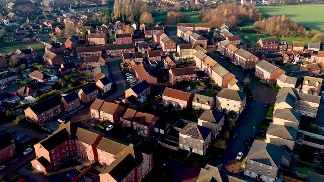 Aerial drone footage of the town of Batley in Wakefield in the UK, showing a typical British housing estate with rows of houses and homes near a public playing field on a sunny day in the winter time