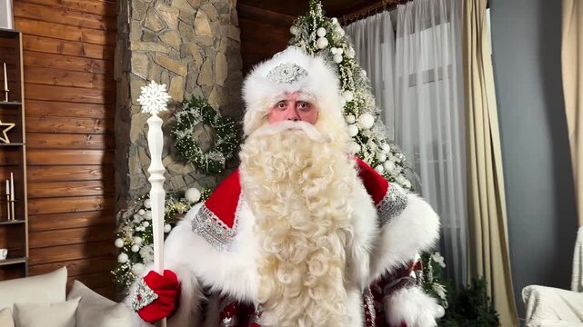 Father Frost, with a sly squint, taps his staff and speaks against the backdrop of a decorated New Year's tree.