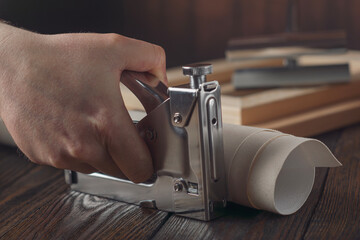 Hand holding stapler for stretching canvas with wooden stretcher bars and fabric on textured table.