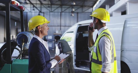 Talking supervisor in suit and foreman in hi-vis vest loading cargo in garage, clipboard and radio