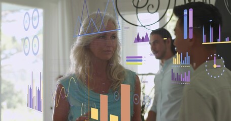 Holding wine glass, senior woman wearing teal top listening at home, showing digital charts