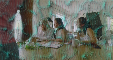 Sitting four women reviewing documents at office meeting table wearing business casual teal overlay