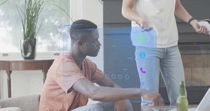 Reaching seated man wearing tee and jeans using hologram controls at home, standing with smartphone